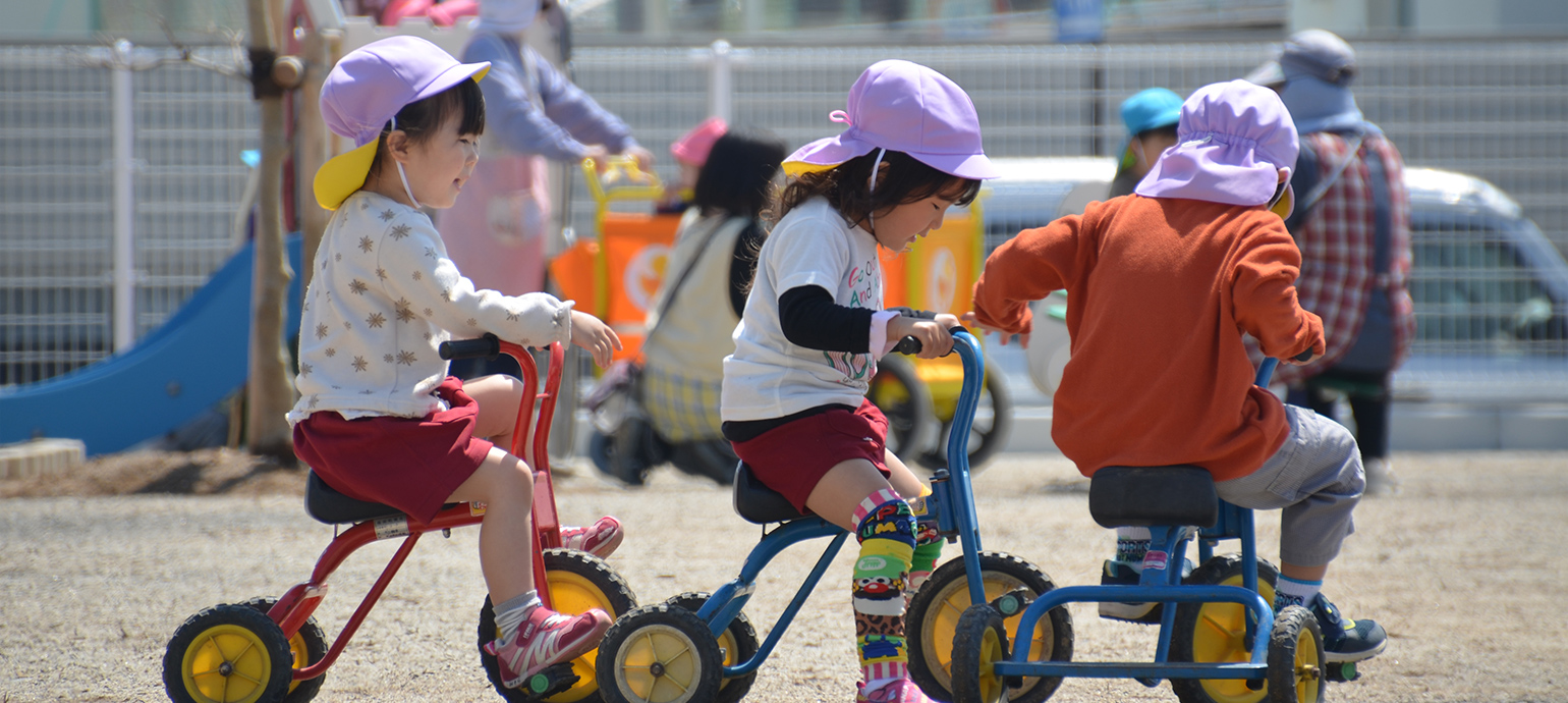 写真：三輪車を楽しそうに漕いで遊ぶ園児たち